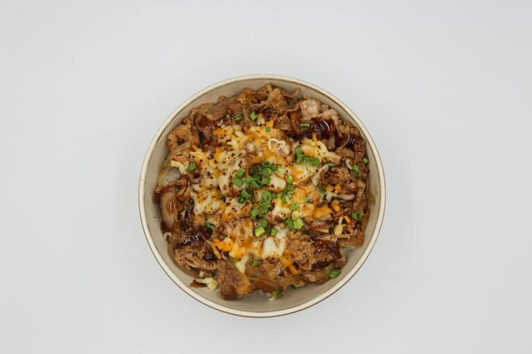 Top view of a savory beef rice bowl with melted cheese and green onions on a white background.