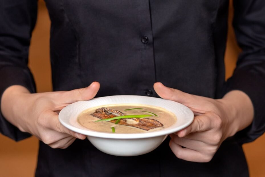 Close-up of a person holding a bowl of creamy mushroom soup with garnish.