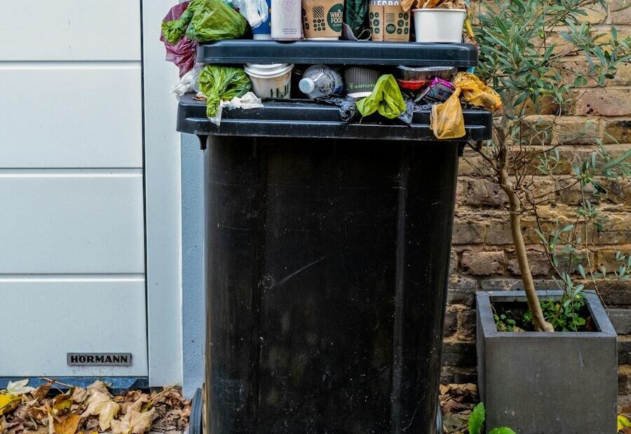 An overflowing black plastic trash bin filled with coffee cups and plastic bags